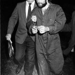 Flanqueado por dos detectives del Escuadrón de Homicidios del Condado de Suffolk, Ronald DeFeo, de 24 años, es llevado a su arresto por múltiples cargos de asesinato en Hauppauge, Nueva York, el 11 de noviembre de 1974.