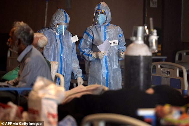 Los trabajadores de la salud que usan equipo de protección se paran junto a un paciente con coronavirus Covid-19 dentro de un salón de banquetes convertido temporalmente en un centro de atención de Covid en Delhi el lunes.