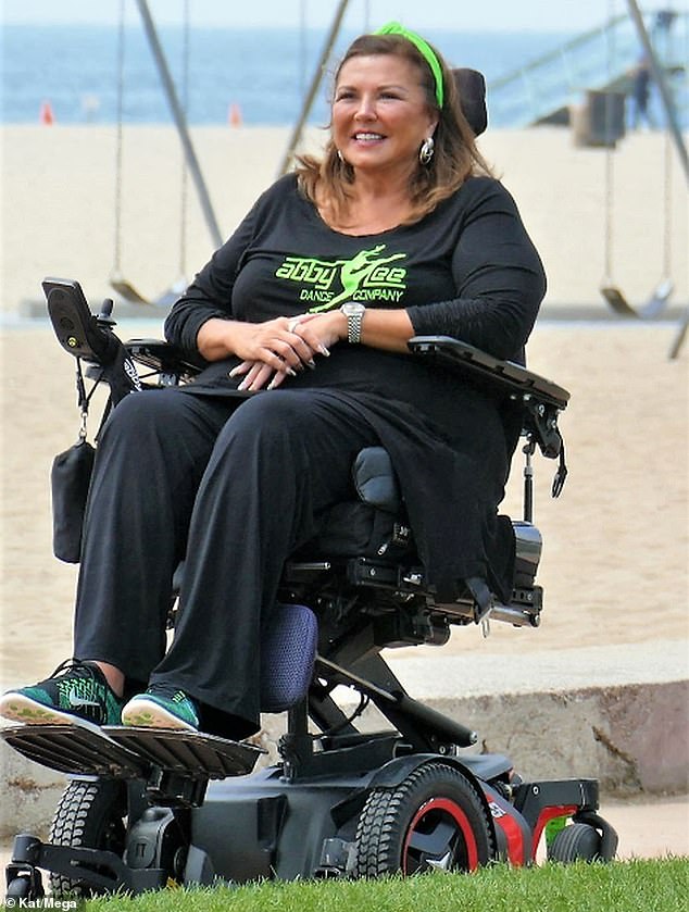 Abby Lee Miller de Dance Moms se recuesta en su silla de ruedas mientras una gimnasta da volteretas sobre ella