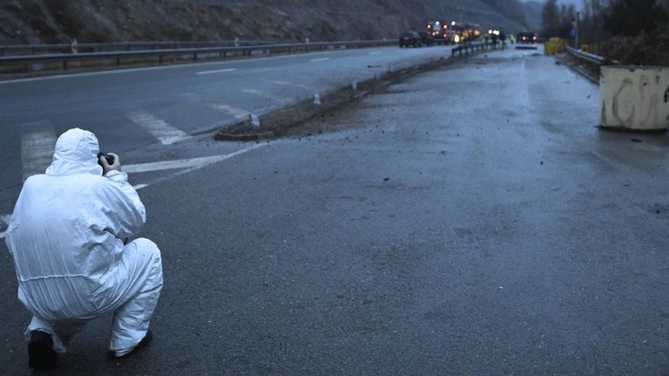 Un investigador toma una fotografía de los restos de un autobús con placas de Macedonia del Norte que se incendió en una carretera.