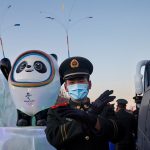 Un oficial de policía paramilitar hace un gesto al fotógrafo frente a la mascota de los Juegos Olímpicos de Invierno de Beijing 2022