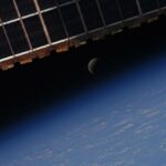 Image shows the lunar eclipse framed by the solar panels of the international space station above and the earth below it.