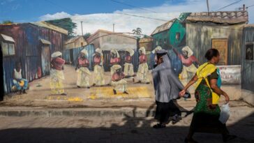 Two women walk in front of a mural with traditional drawings depicting the culture and history of the Mafalala neighbourhood in Maputo on April 21, 2022.