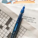 Blue pen rests on a newspaper that has a partially filled out crossword puzzle