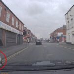 Cuando el automóvil se detiene en un semáforo en rojo en Ribbleton Road, en Preston, Lancashire, el conductor imprudente corre hacia adelante con el niño colocado de manera insegura a sus pies.