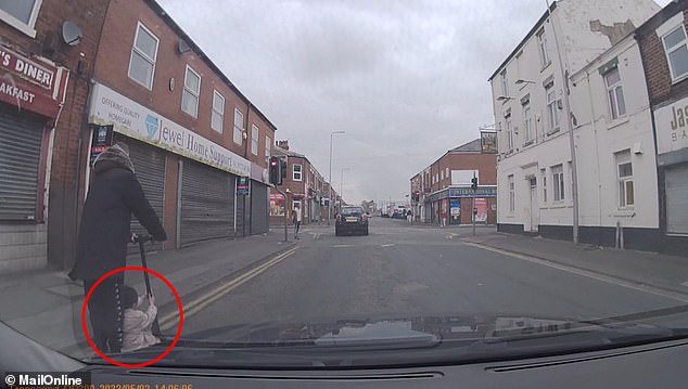 Cuando el automóvil se detiene en un semáforo en rojo en Ribbleton Road, en Preston, Lancashire, el conductor imprudente corre hacia adelante con el niño colocado de manera insegura a sus pies.