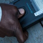 A man puts his thumb on a biometric machine to check his ID to cast his vote at a polling station in Kampala, Uganda, on January 14, 2021.