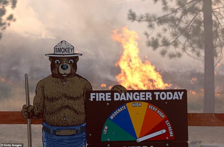 A pesar de los esfuerzos de más de 2,000 bomberos para contener las llamas, el fuego, que comenzó el viernes en las laderas de Sierra Nevada, estaba contenido en un 0 por ciento el domingo, dijeron los bomberos estatales.  En la imagen se muestra el fuego furioso detrás de un cartel de advertencia de Smokey the Bear contra incendios forestales el domingo.