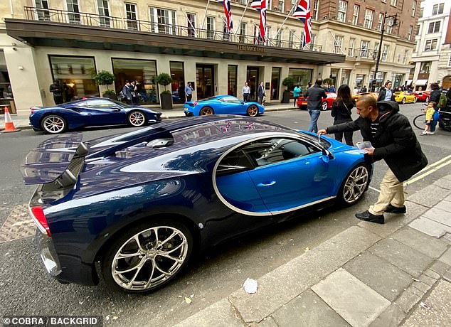 Un hombre recoge lo que se entiende como una multa del parabrisas de un Bugatti Chiron de 2,4 millones de libras fuera del exclusivo hotel de cinco estrellas May Fair en Londres.