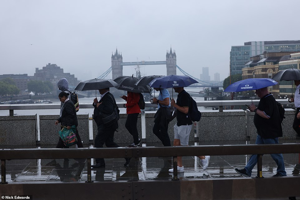 Los viajeros se refugian bajo los paraguas mientras cruzan el Puente de Londres bajo la fuerte lluvia y las tormentas eléctricas esta mañana.