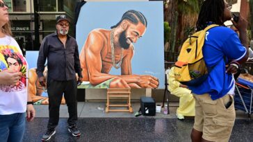 Artist Mohammed Mubarak stands beside his artwork of the late US rapper Nipsey Hussle as people gather for Hussle's posthumous Hollywood Walk of Fame Star ceremony in Hollywood, California, on August 15, 2022. - Slain rapper Nipsey Hussle, who was shot in Los Angeles three years ago, was honored with a star on Hollywood's Walk of Fame on what would have been his 37th birthday. (Photo by Frederic J. BROWN / AFP) (Photo by FREDERIC J. BROWN/AFP via Getty Images)