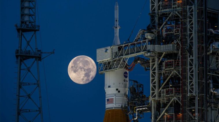 A full moon behind the Space Launch System rocket and Orion spacecraft during testing for the Artemis I mission.