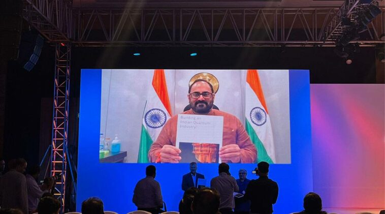 Rajeev Chandrashekhar on a projector screen hlding up paper that says "Building an Indian Quantum industry"