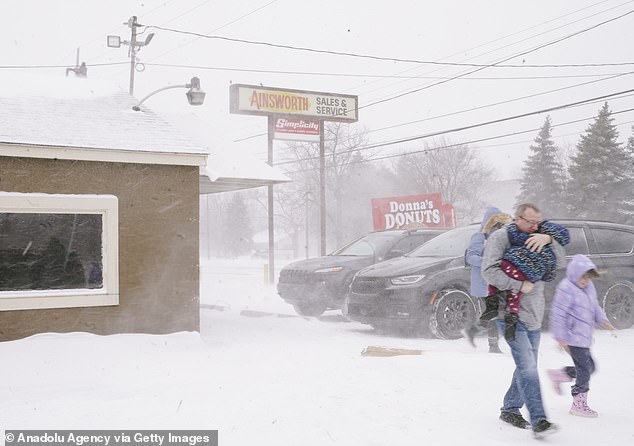 Se ve a una familia corriendo hacia su automóvil en Flint, Michigan, el viernes en medio de condiciones de ventisca.