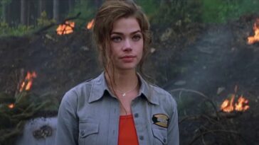 Denise Richards stands at an explosion site, looking annoyed in The World is Not Enough.