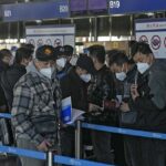 Los viajeros enmascarados revisan sus pasaportes mientras hacen fila en el mostrador de facturación en el aeropuerto internacional de Beijing Capital hoy.