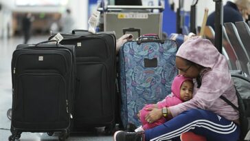 Una pasajera varada sostiene a su hija de 14 meses mientras espera con familiares en la terminal suroeste del Aeropuerto Internacional de Los Ángeles el martes.
