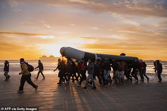 Los traficantes de personas están ofreciendo transportar a los inmigrantes a través del Canal en botes peligrosamente superpoblados por menos de £ 500 como un trato de Navidad a precio reducido.  En la imagen: Migrantes cargando un bote de contrabando mientras se preparan para cruzar el Canal de la Mancha en octubre.