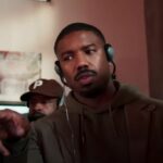 Michael B. Jordan pointing at a monitor and wearing headphones while directing Creed III