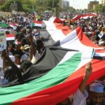 Sudanese protesters deploy a giant national flag, as they march outside the UN headquarters in the Manshiya district of the capital Khartoum, on December 3, 2022.