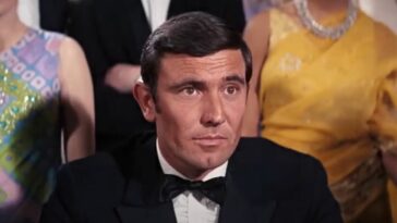 George Lazenby sitting in front of a crowed, dressed in a tuxedo in On Her Majesty