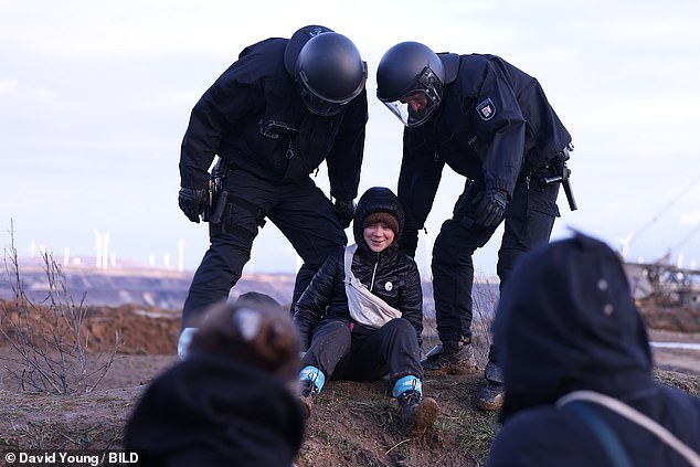 Se ve a Greta Thunberg sonriendo mientras está rodeada por dos policías en Lutzerath en Alemania hoy.