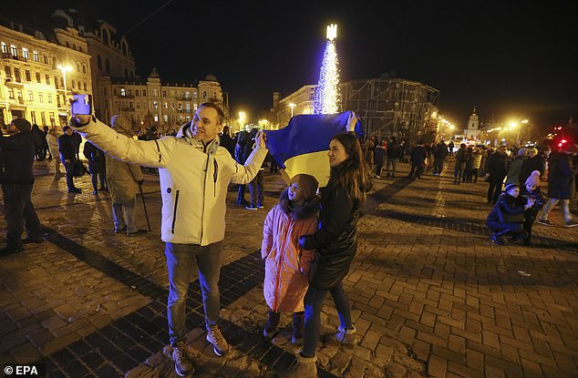 Los ucranianos se toman una selfie con la bandera nacional ucraniana cerca de un árbol de Navidad por la noche en el centro de Kyiv, Ucrania, el 31 de diciembre de 2022 antes del Año Nuevo