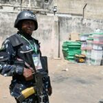 A Nigerian anti-riot Police officer stands metres away from ballot boxes.