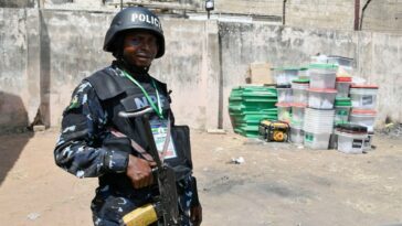 A Nigerian anti-riot Police officer stands metres away from ballot boxes.