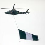 A military helicopter carries the Nigerian flag during the inauguration of President Bola Ahmed Tinubu in May 2023. (Photo by KOLA SULAIMON / AFP)