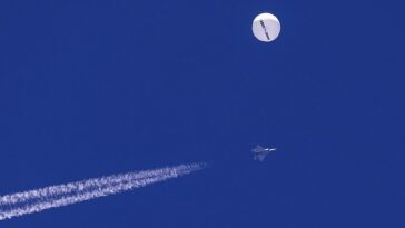 El globo espía se ve a la deriva sobre el Océano Atlántico, frente a la costa de Carolina del Sur, el sábado, con un avión de combate y su estela debajo de él.