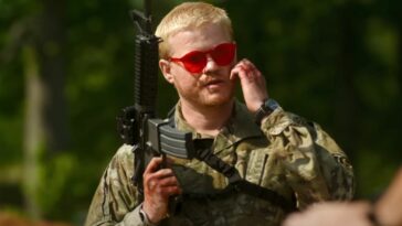 Jesse Plemons holds a gun in one hand while scratching his face with another in Civil War.