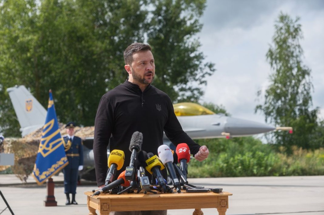 President Volodymyr Zelensky stands in front of a F-16 Fighting Falcon jet.