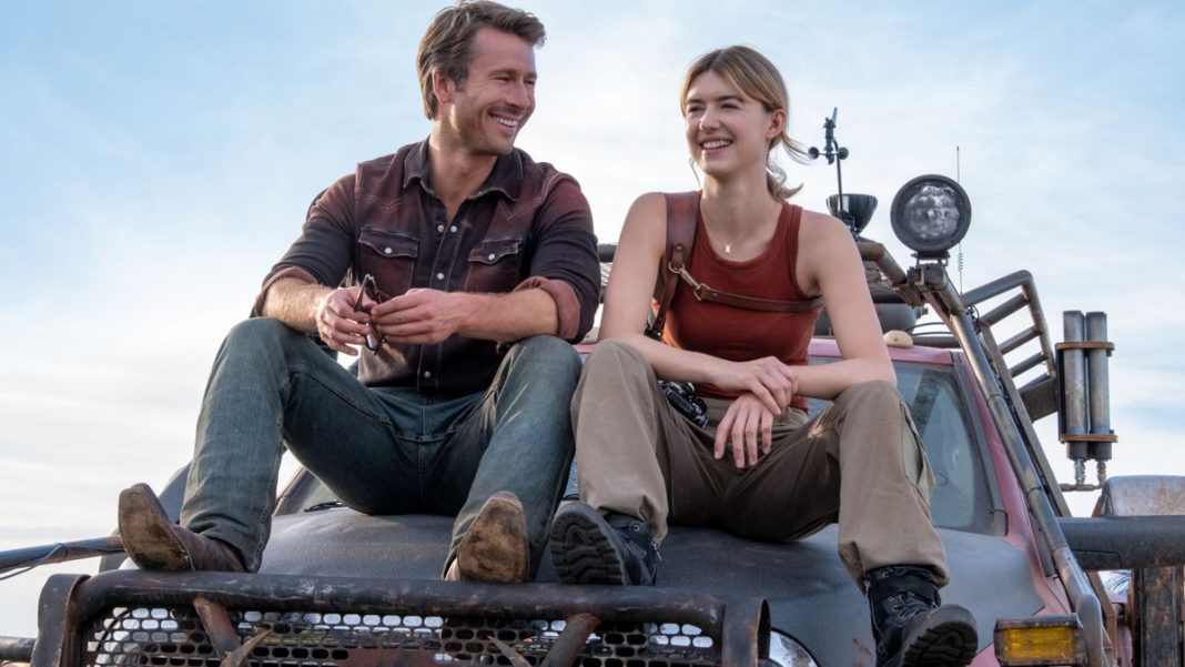 Glen Powell and Daisy Edgar-Jones smiling together while sitting on top of a truck