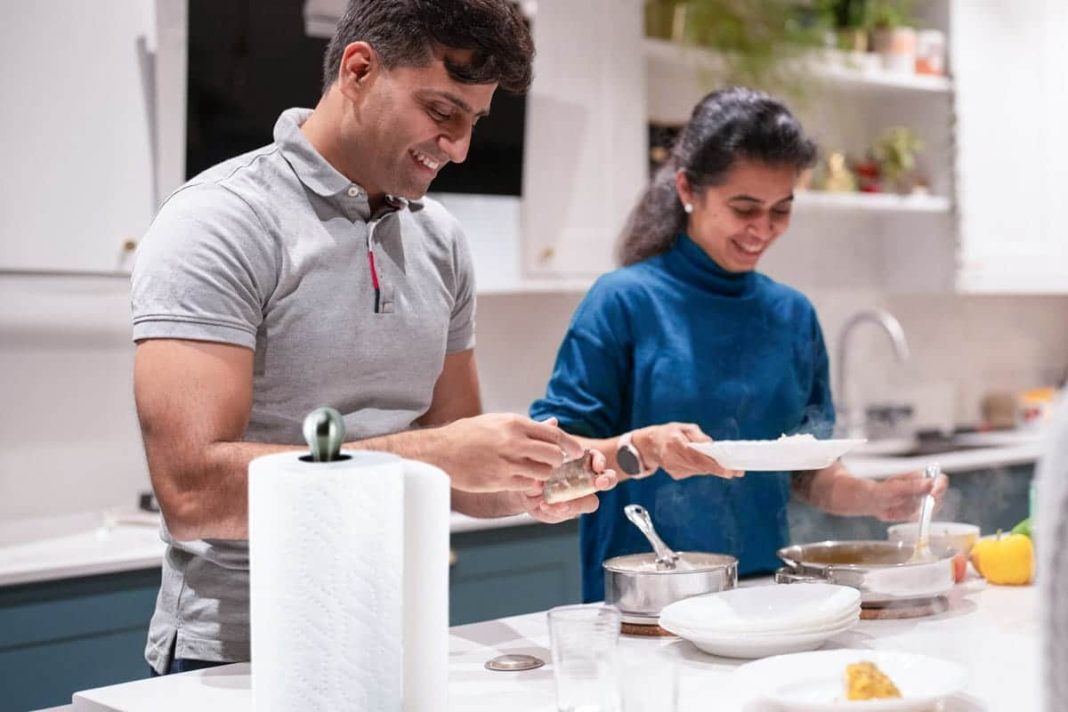 A man and a woman stand next to a kitchen counter while cooking, with a paper towel next to them.