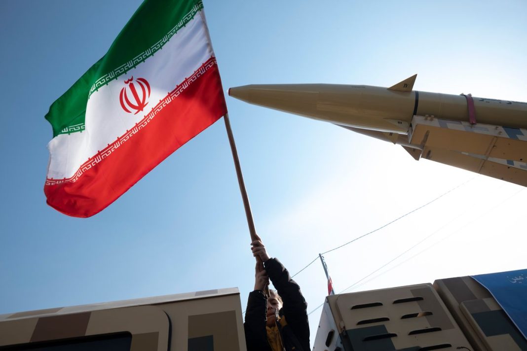 A young boy is waving an Iranian flag next to the Iranian-made Zolfaghar missile