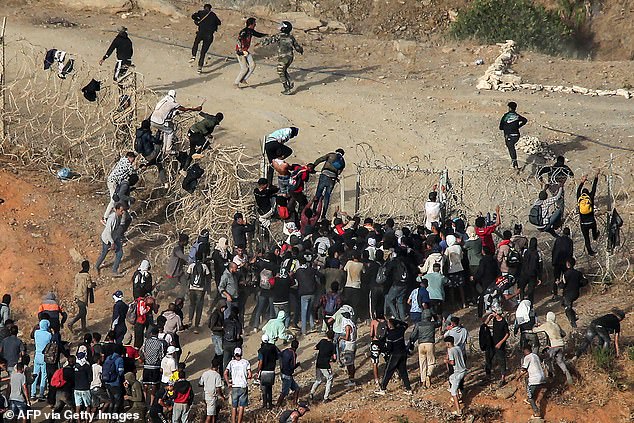 Los migrantes asaltan una valla de alambre de púas cuando intentan cruzar la frontera terrestre con el enclave africano español de Ceuta, cerca de Fnideq, en el norte de Marruecos, el 15 de septiembre