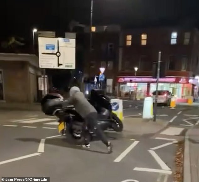 El vándalo encapuchado, vestido de gris, empujó la motocicleta hacia un lado mientras estaba estacionada cerca de una isleta de tráfico en Cheltenham el 12 de noviembre.