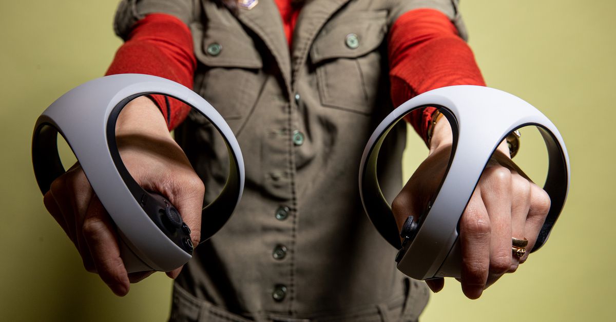 Adi holds both controllers out directly in front of her, towards the camera.