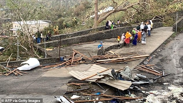 Una foto tomada el 15 de diciembre de 2024 muestra a residentes sentados junto a una carretera entre montones de escombros de láminas de metal y madera después de que el ciclón Chido azotara el territorio francés de Mayotte en el Océano Índico.