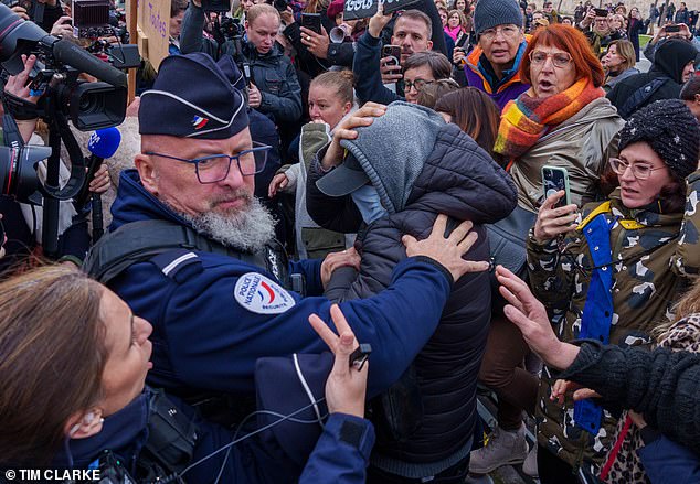 La policía tuvo que proteger al hombre que se escondía detrás de una mascarilla y una capucha de los manifestantes enojados que se burlaban de él.