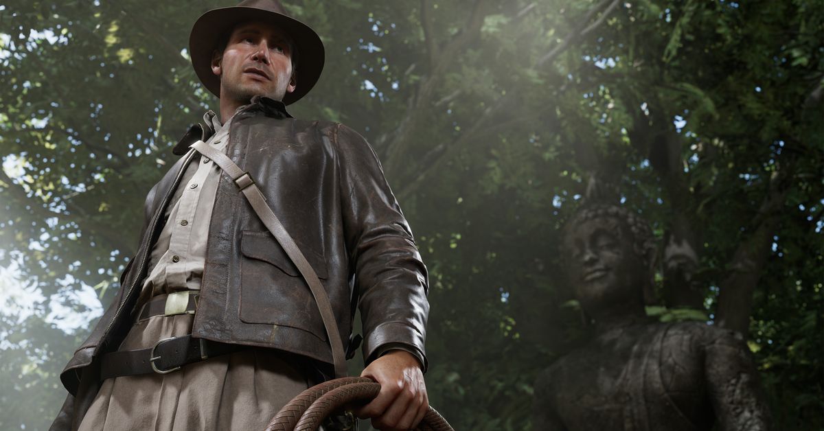 Screenshot from Indiana Jones and the Great Circle featuring a shot of Indiana Jones a white male wearing a brown leather jacket and brown leather hat standing in front of a Buddhist statue.