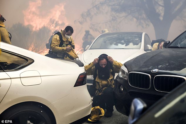 Un BMW y un Tesla se ven en el tráfico abarrotado mientras el fuego arde al fondo.