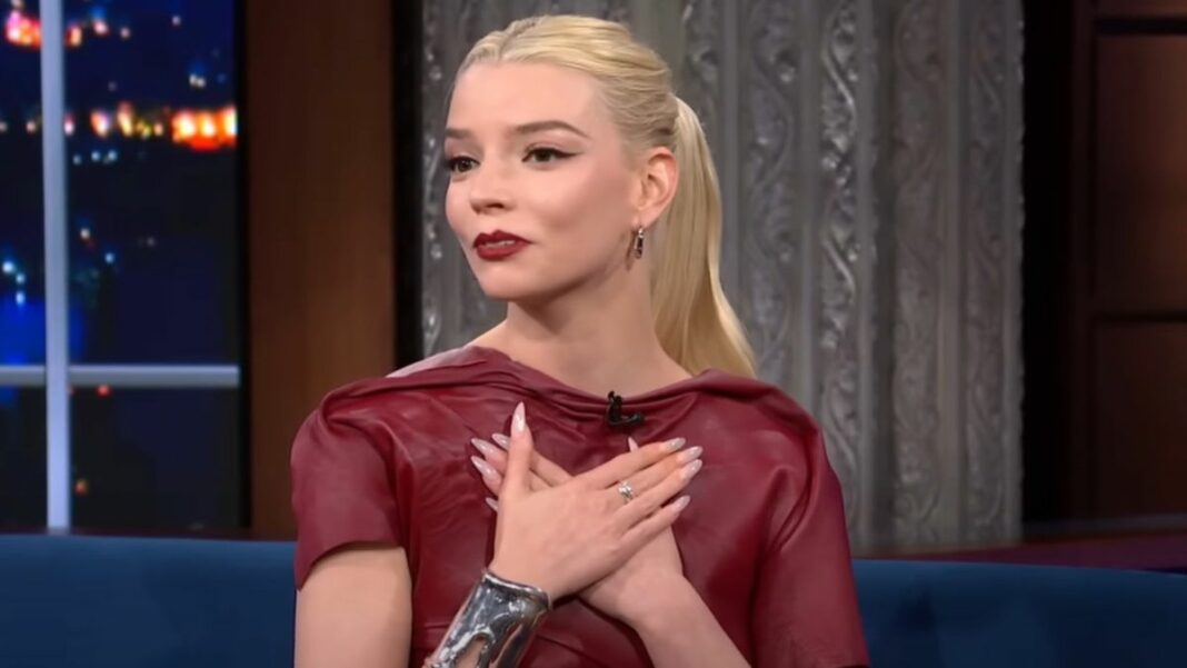 Anya Taylor-Joy smiling and looking affectionate as she places both her hands over her heart.