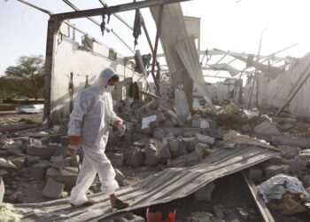 Una persona en equipo de protección camina a través de los escombros de un edificio bombardeado.