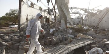 Una persona en equipo de protección camina a través de los escombros de un edificio bombardeado.