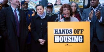 La representante Barbara Lee, rodeada de otros, habla en un podio con un letrero fijo que lee "Manos fuera de la carcasa"