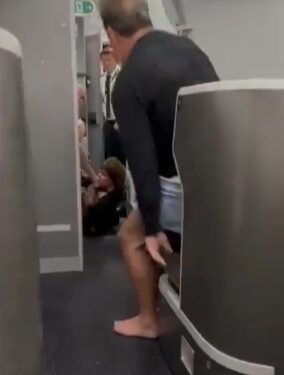Hombre en pantalones cortos y descalzos ayudando a un pasajero en un avión.
