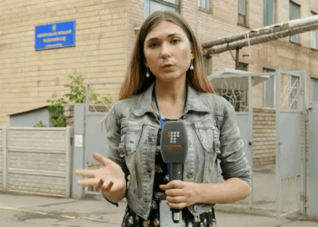 Reportero sosteniendo un micrófono frente a un edificio.