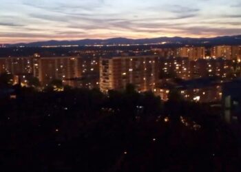 Vista nocturna de edificios de la ciudad y montañas distantes.